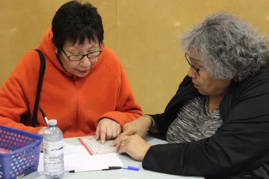 Two women work together, pointing at a paper on a table.