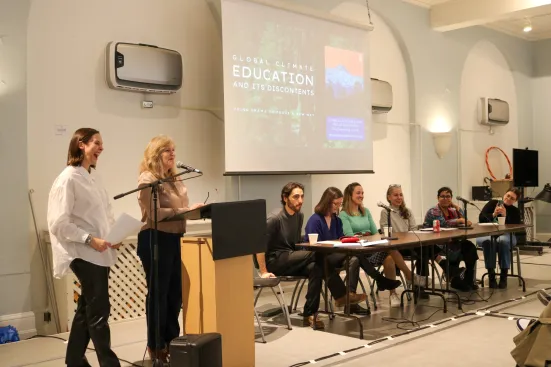 A panel discussion on climate education with eight speakers seated and standing near a projector screen.