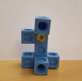 Blue interlocking cubes stacked in an abstract shape with one yellow sticker.