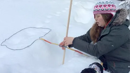 A kid measuring an animal imprint in snow
