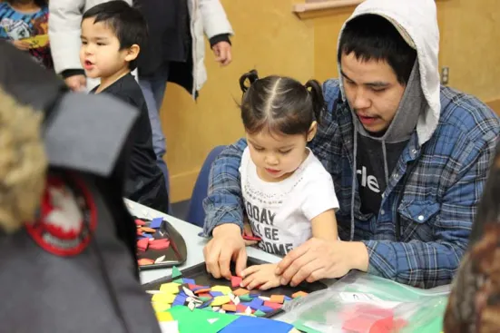 A man helps a young girl arrange colorful foam shapes at a table.