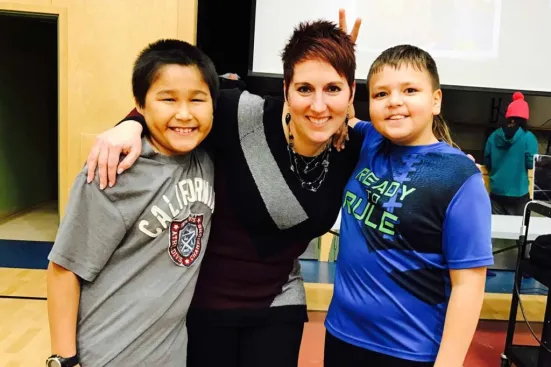 A woman poses with two smiling boys, one playfully giving her bunny ears.