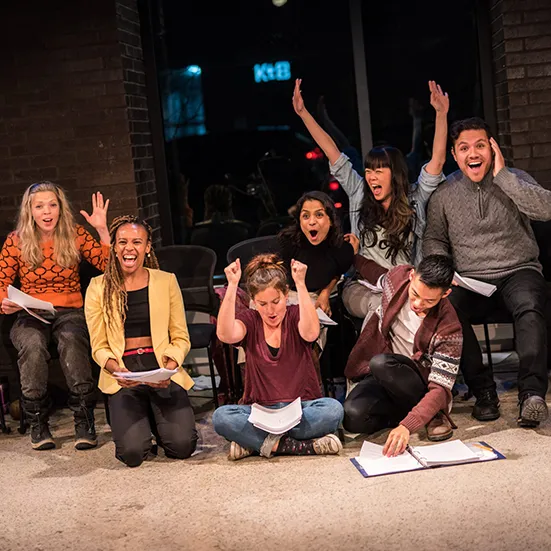 Cast of Towards Youth celebrating with their arms raised during a rehearsal