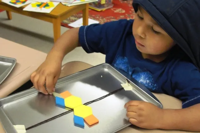 A kindergarten student uses a cookie sheet and magnetic pattern blocks to create symmetry.