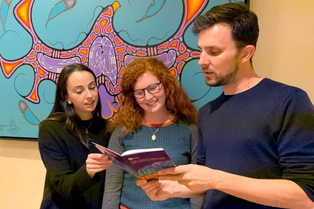 Three people looking at a book.