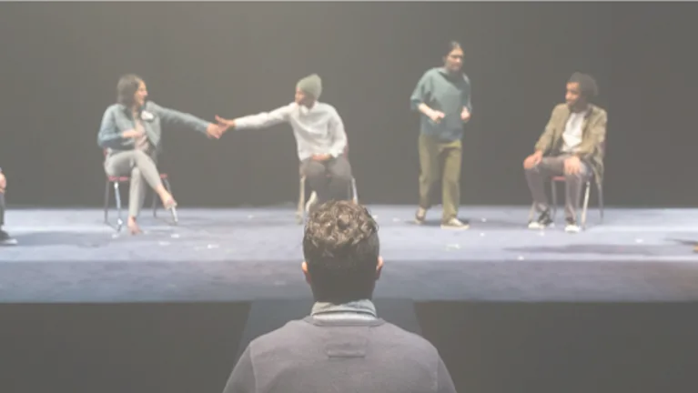 The back of a person's head in the foreground, watching a stage of actors.