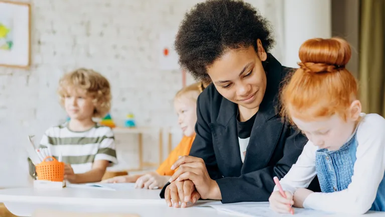 An instructor helping a student with homework. Another child is seated in the background.
